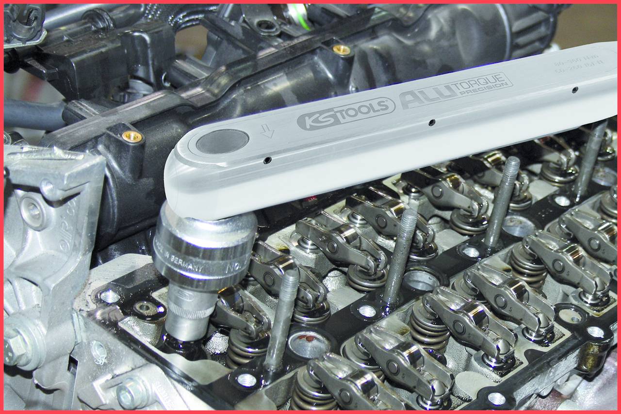 Close-up van een motor met een momentsleutel die aan een klepdeksel werkt. De focus ligt op de mechanische onderdelen.