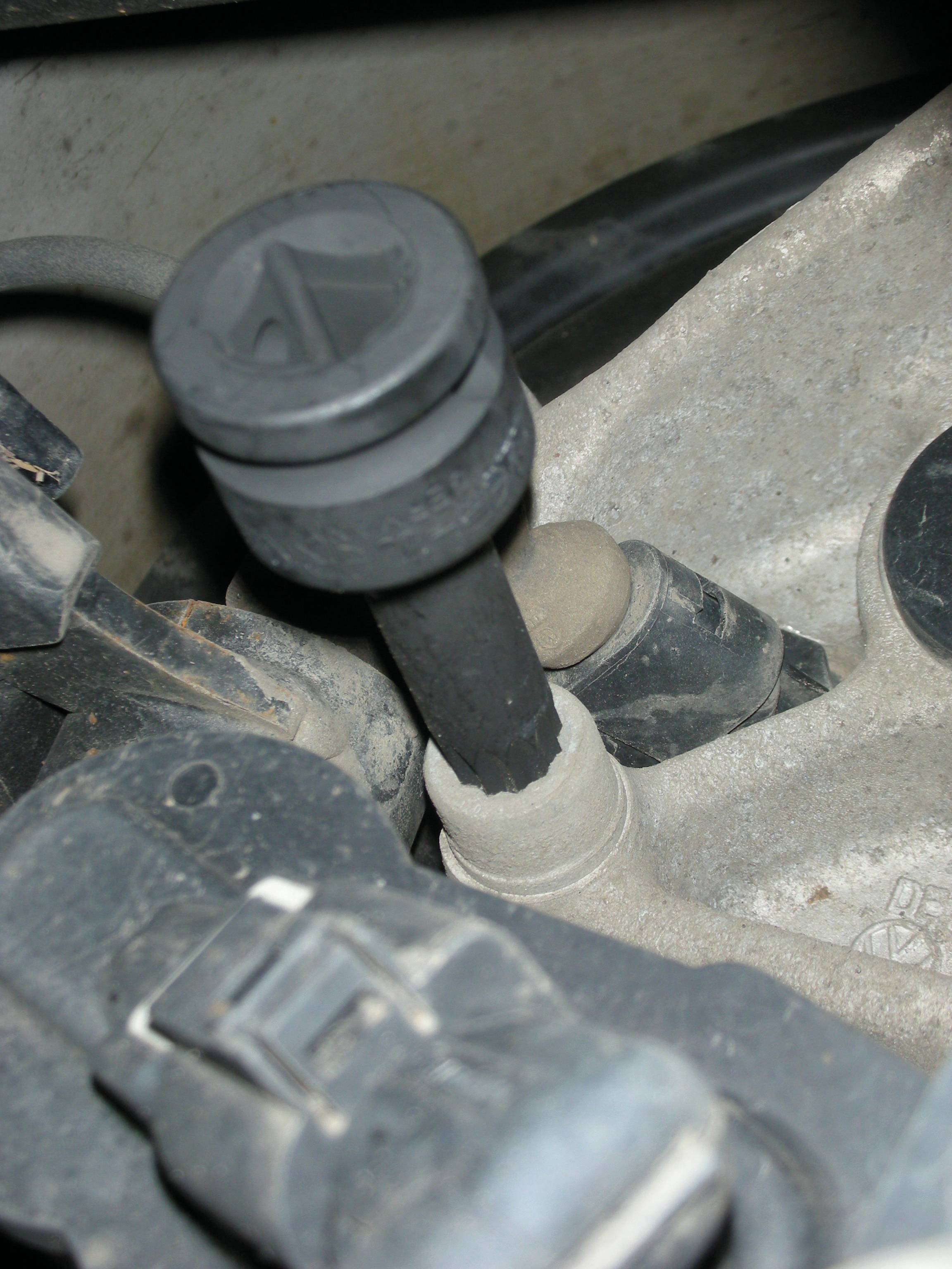 Close-up van een zwart autoonderdeel met een hefboom op een metalen oppervlak, waarschijnlijk deel van een versnellingsbak of motorverbinding.