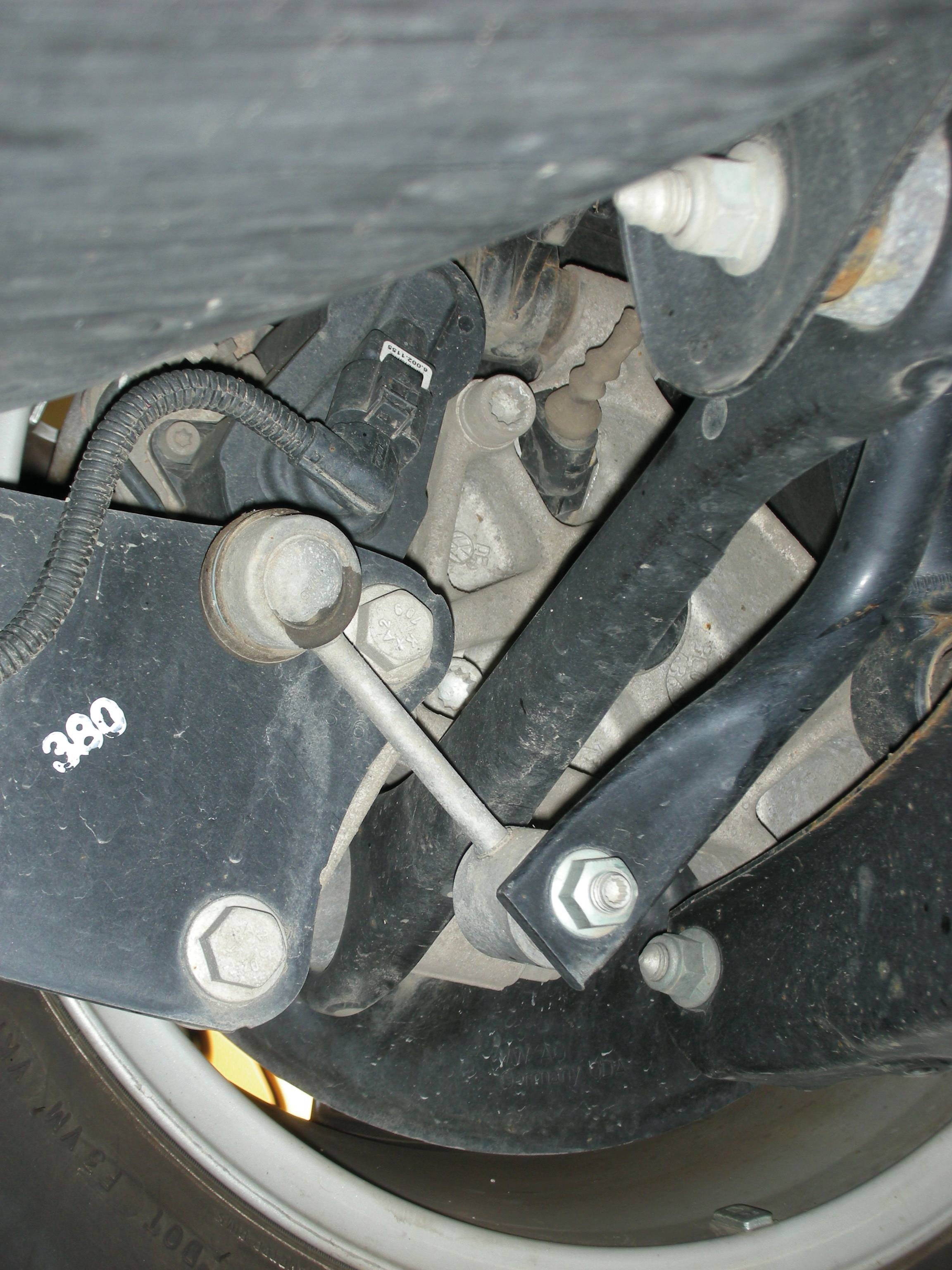 'Close-up van een auto-onderdeel onder een voertuig. Zichtbaar zijn metalen componenten, schroeven en kabels met een aanduiding "380".'