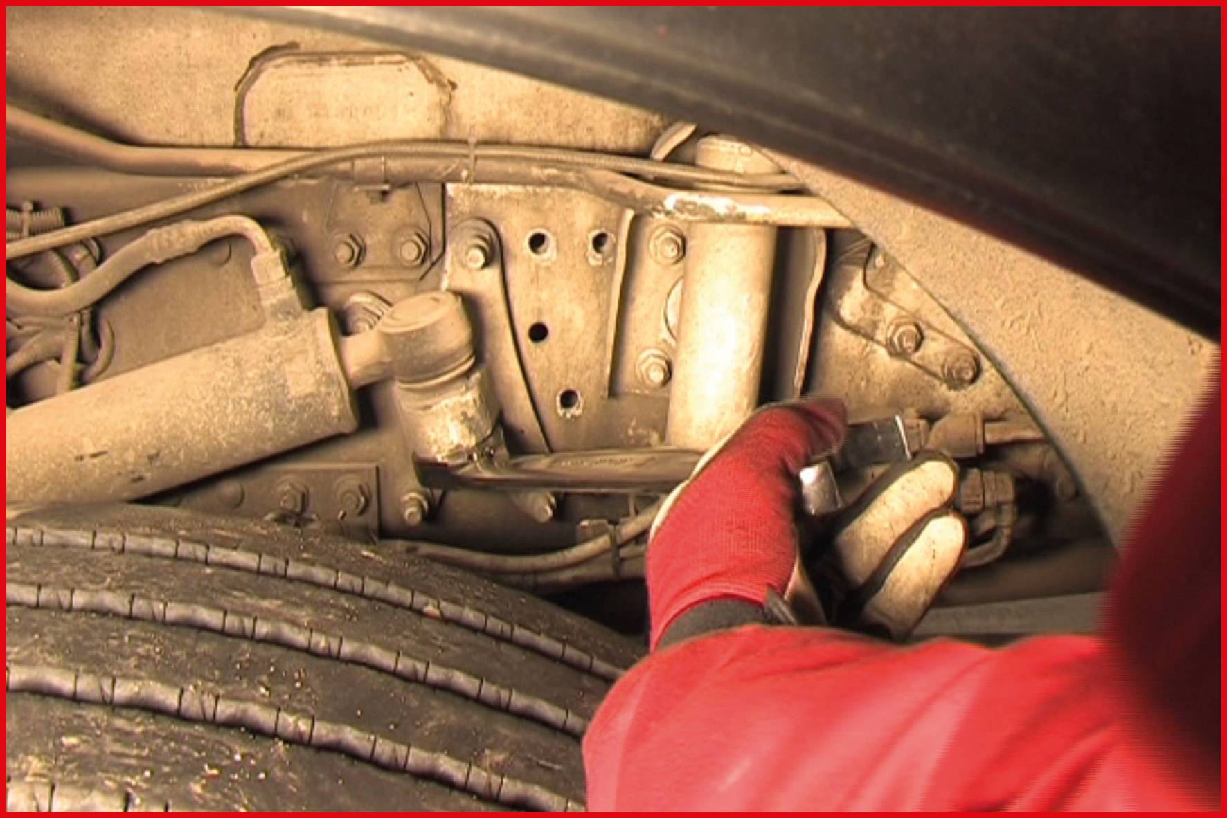 'Close-up van een monteur in een rode overall en handschoenen die werkt aan de wielophanging van een voertuig.'