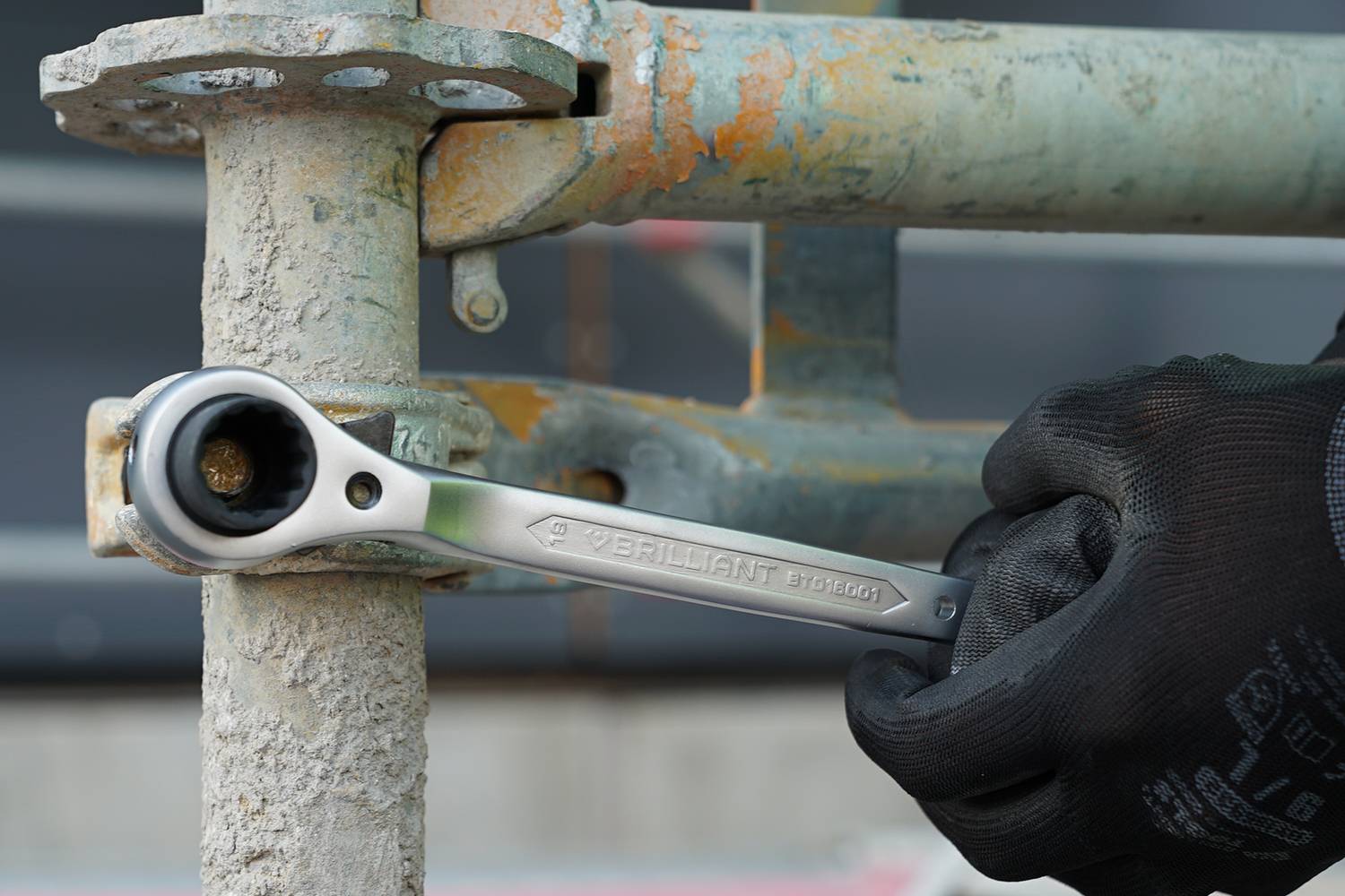 Een arbeider met zwarte handschoenen draait een schroef vast aan een metalen frame met behulp van een zilveren moersleutel.