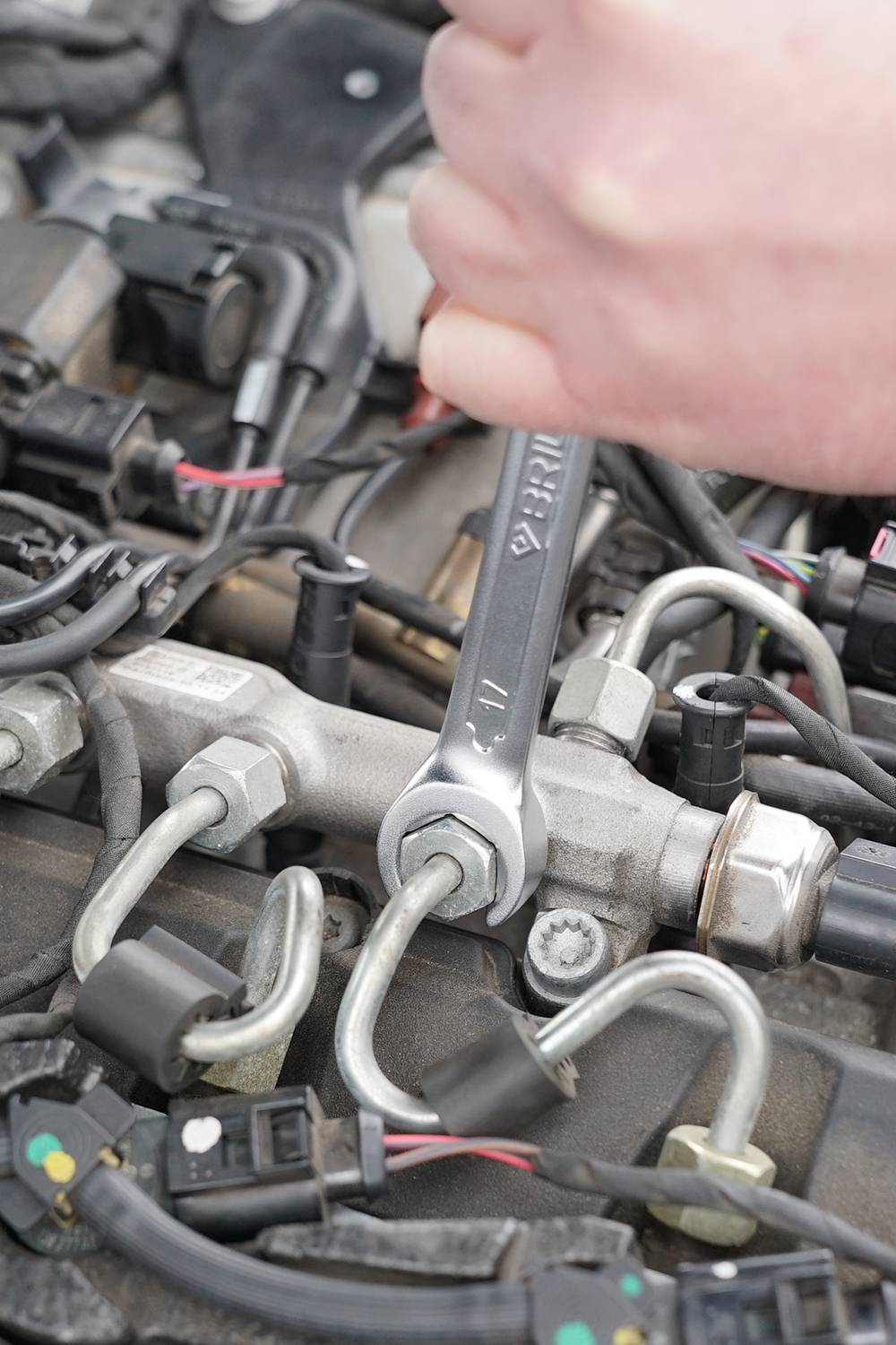 Een hand repareert een motor met een moersleutel. Verschillende draden en schroeven zijn zichtbaar.