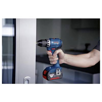 Een persoon houdt een blauw en zwart snoerloos boormachine nabij een metalen oppervlak in een moderne ruimte, wat wijst op doe-het-zelf of renovatiewerkzaamheden.