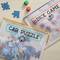 Twee doorzichtige tassen met rits: Eén bevat gekleurde dobbelstenen met het opschrift 'Dice Game', de andere puzzelstukken met 'Car Puzzle'.