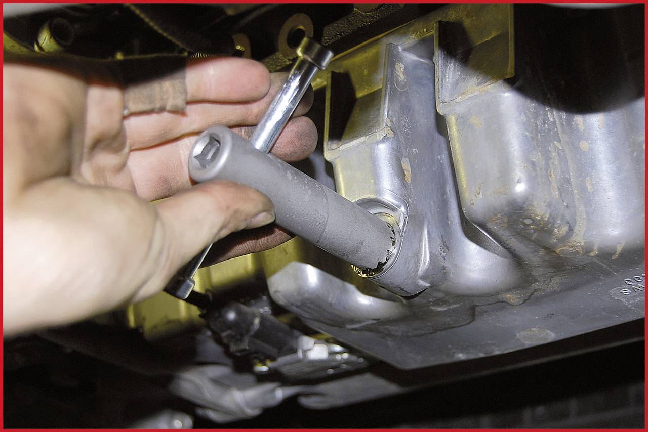 Een monteurhand gebruikt een gereedschap om een schroef los te draaien op een metalen oppervlak, vermoedelijk aan een voertuigmotor of machine.