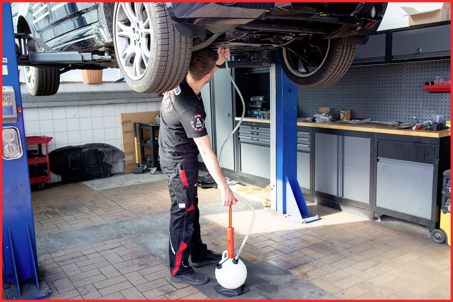 Een monteur werkt in een garage aan een auto die op een hefbrug staat.