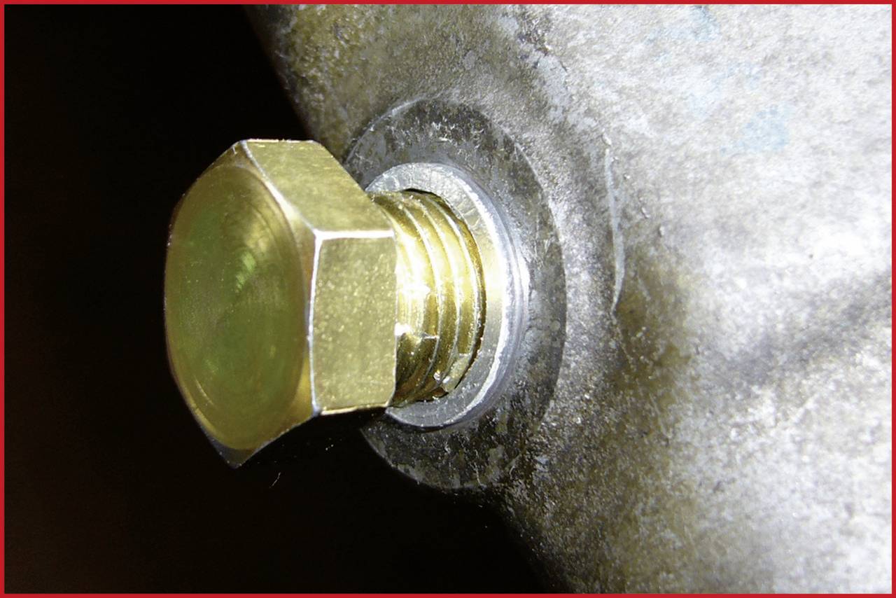 Een gouden zeskantmoer is bevestigd op een zilveren metalen oppervlak. De moer is stevig in de schroefdraadopening vastgedraaid.