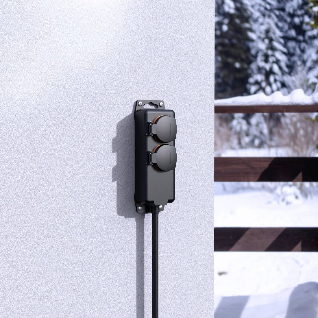 Een buitenstopcontact met twee aansluitingen gemonteerd aan een witte muur, met sneeuw en een houten hek op de achtergrond.