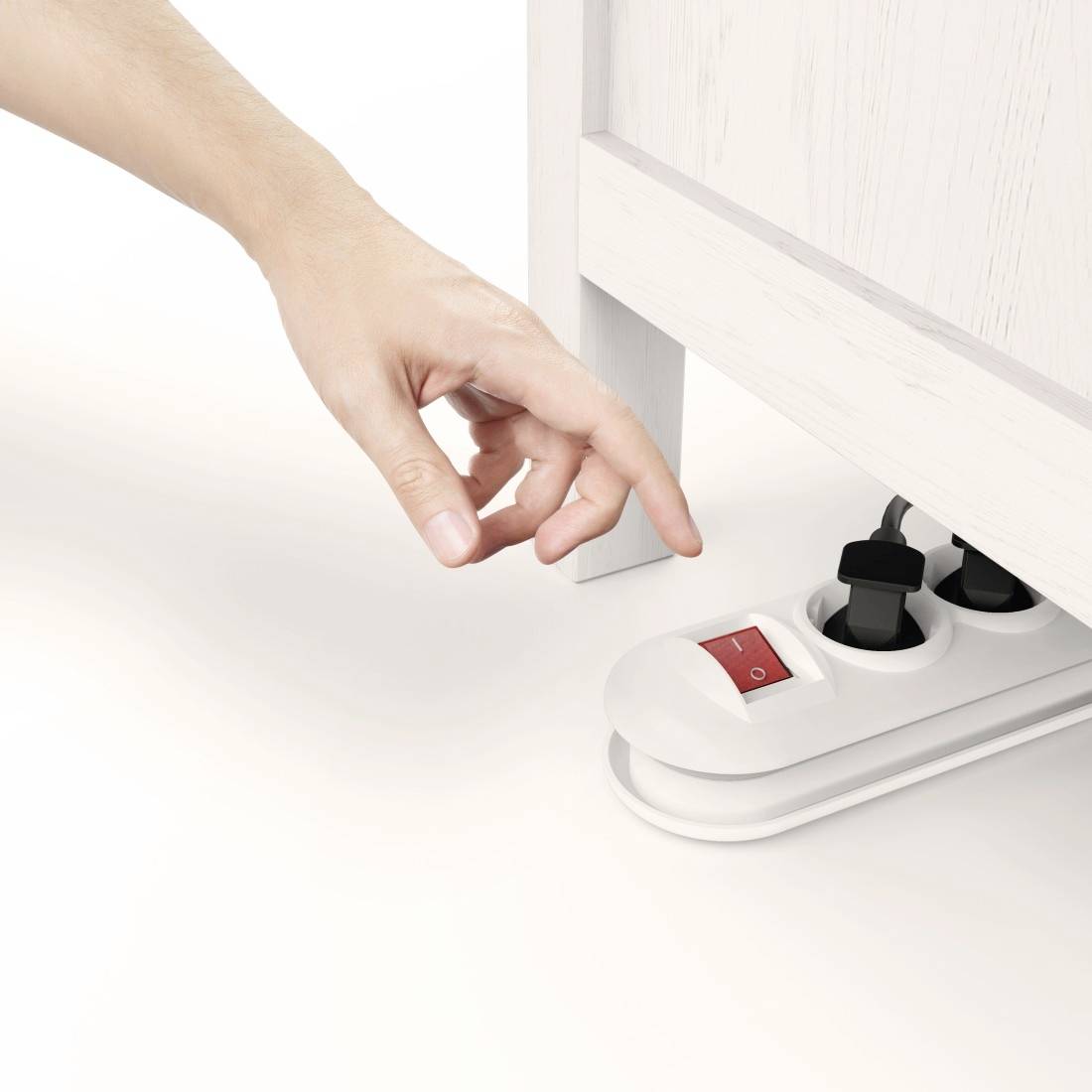 Een persoon schakelt een witte stekkerdoos met een voetschakelaar in onder een kast.