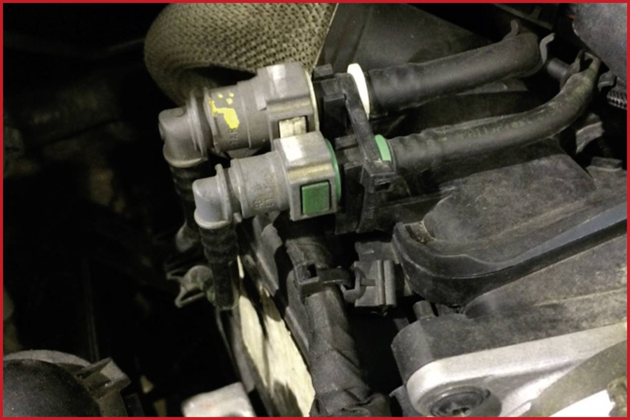 Twee verbonden sensoren met kabels in een motorruimte. Eén heeft groene markeringen, de ander gele. Ze zijn zichtbaar in close-up.