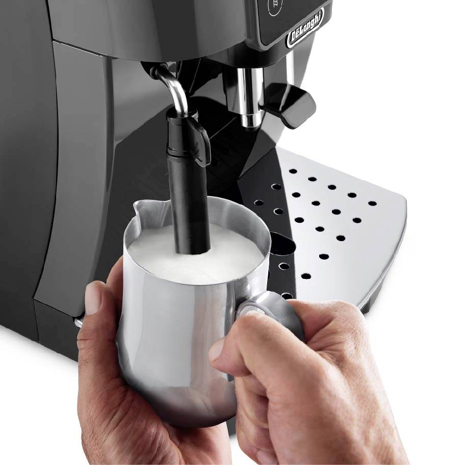 Koffiemachine met melkopschuimer, die melk opschuimt in een metalen kan. Handen houden de kan vast.
