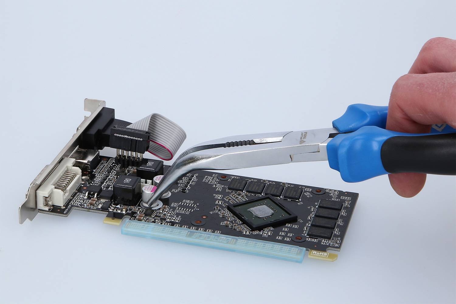 Een hand met blauwe tang manipuleert een computervideokaart op een witte achtergrond.