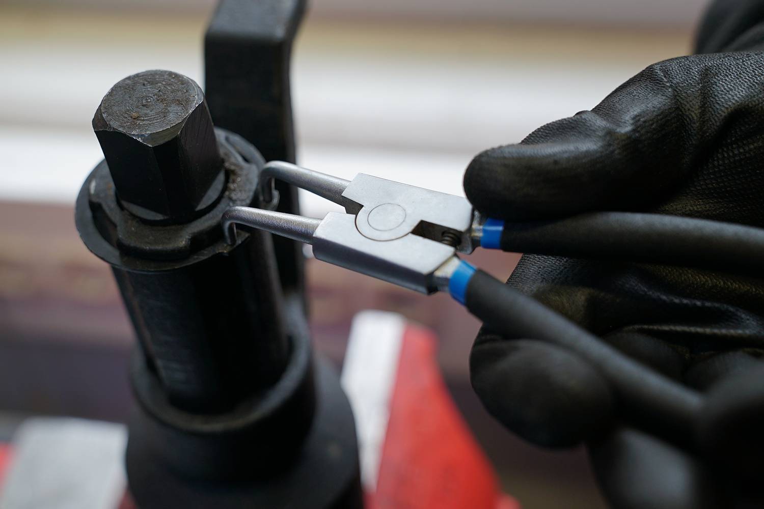 Een persoon met een zwarte handschoen gebruikt een tang om een schroef aan een gereedschap bij te stellen.