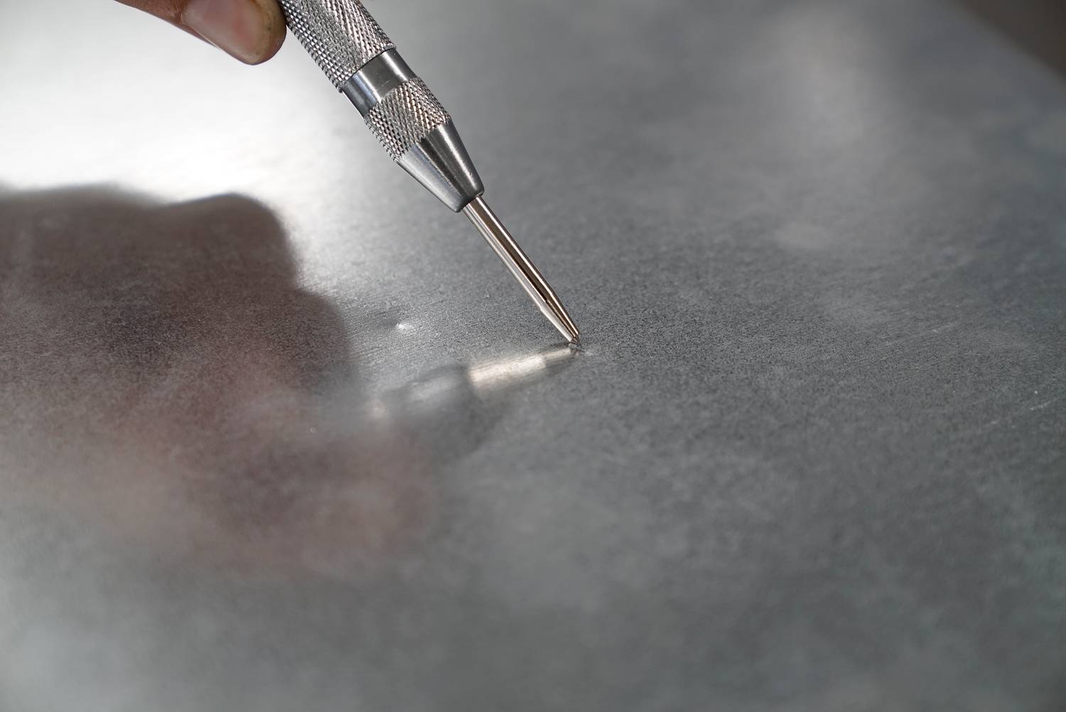 Een hand houdt een metalen pen vast die op een metalen plaat wordt gezet om een markering aan te brengen.