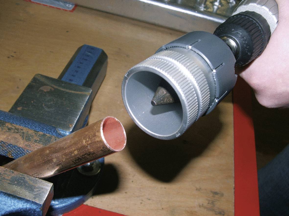 Metalen buis vastgeklemd in een bankschroef. Persoon houdt een ontbraammgereedschap vast.