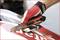 Een hand met rode handschoenen houdt een stanleymes vast, gepositioneerd op een rood-witte ondergrond.