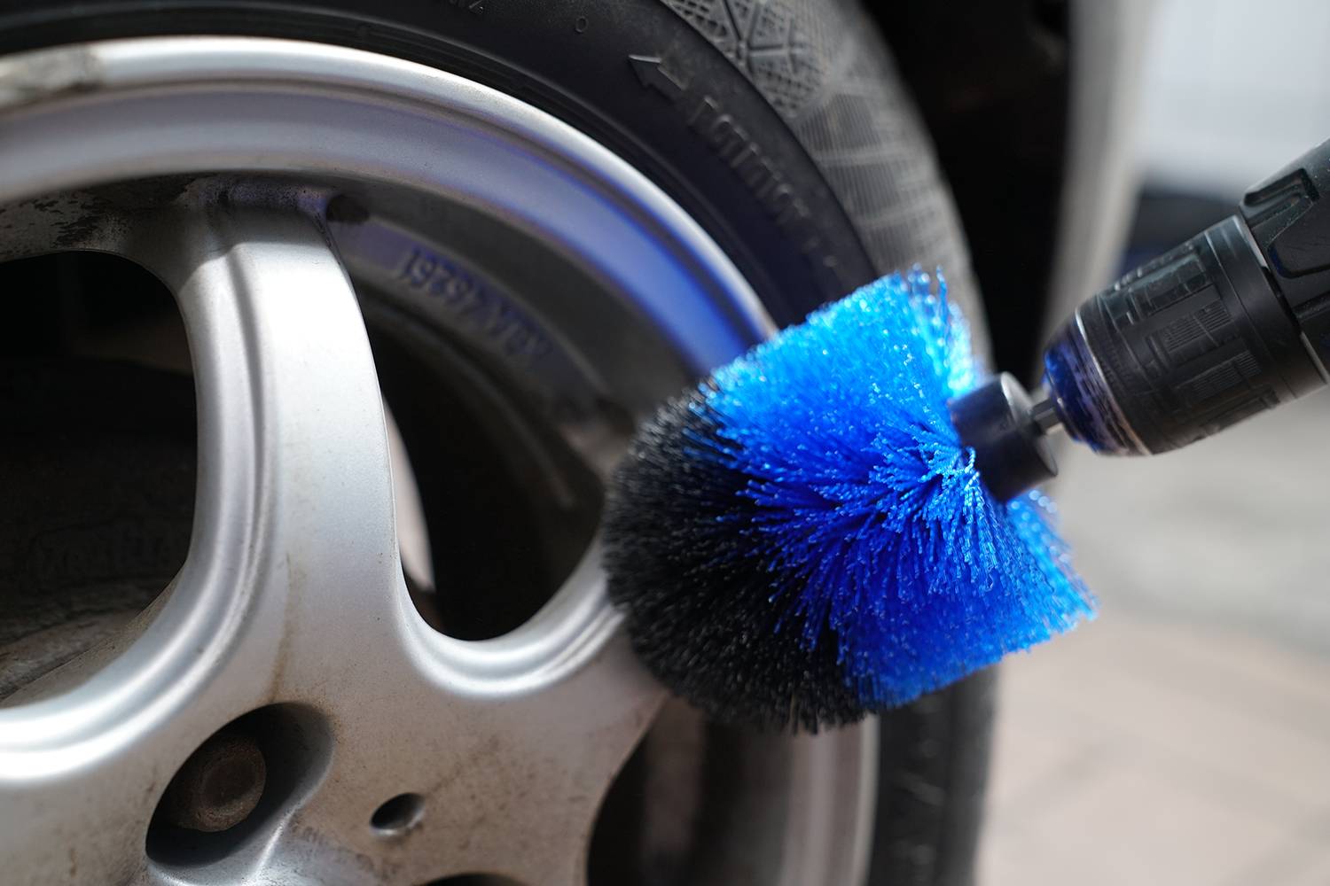 Een roterende borstel met blauwe borstels reinigt de velgrand van een autoband. De focus ligt op de reinheid van de velg.