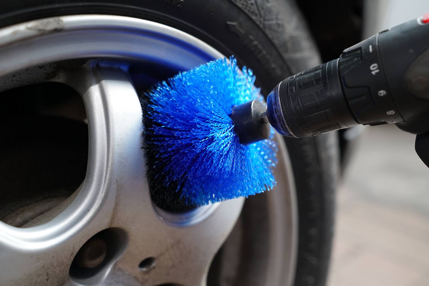 Een autoband wordt met een blauwe borstel in een boormachine gereinigd; close-up toont de reinigingsactie.