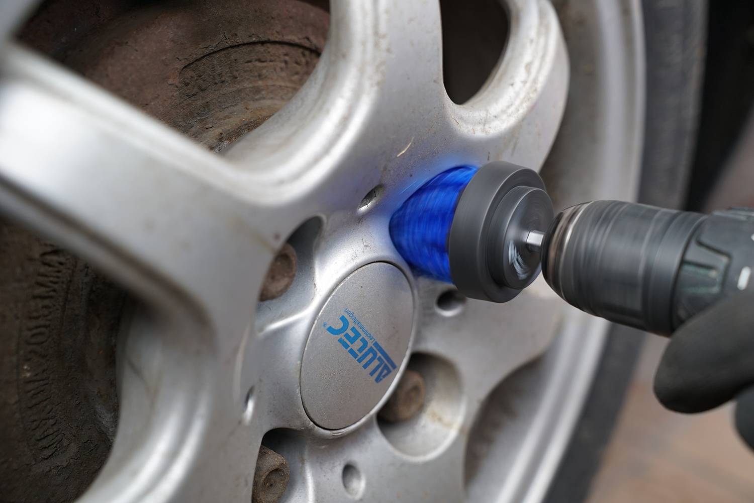 Een monteur polijst een autovelg met een blauwe polijstschijf en een boormachine.