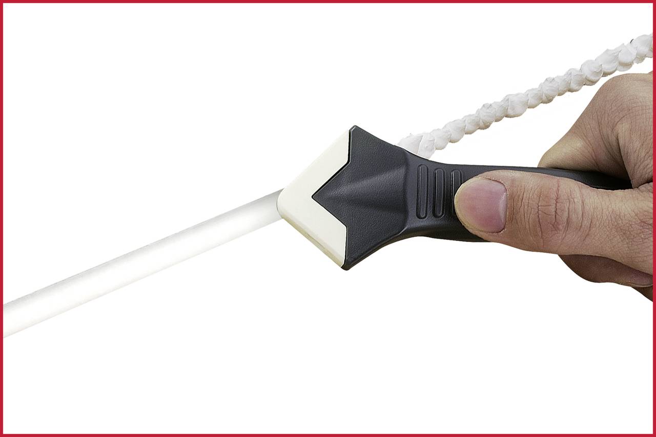 Een hand houdt een gereedschap vast dat een witte dichting verwijdert. Het wordt gebruikt aan een recht buizensysteem.