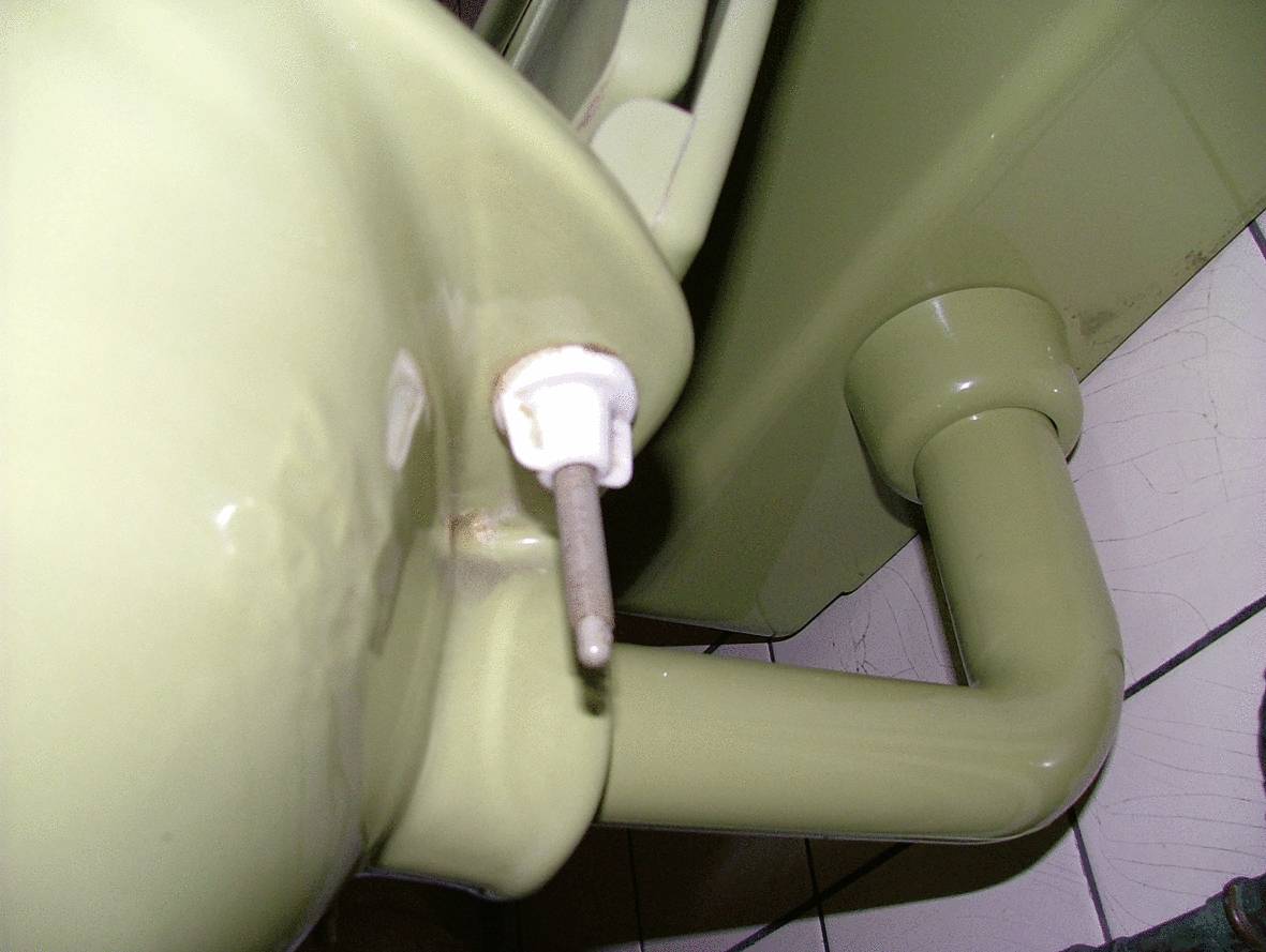 Een oud, olijfgroen wastafel met zichtbare afvoerbuis en wandbevestiging, gemonteerd op witte tegels in de badkamer.