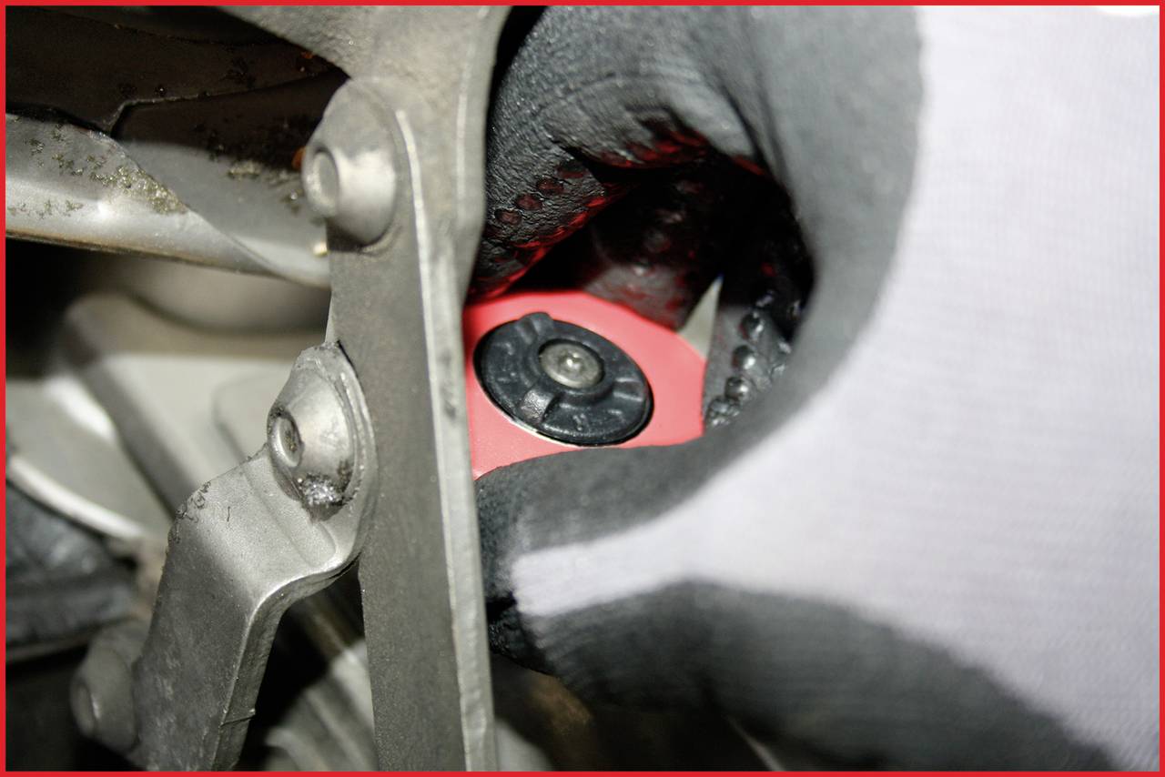'Hand in handschoen draait rode dop aan een mechanisch apparaat'.