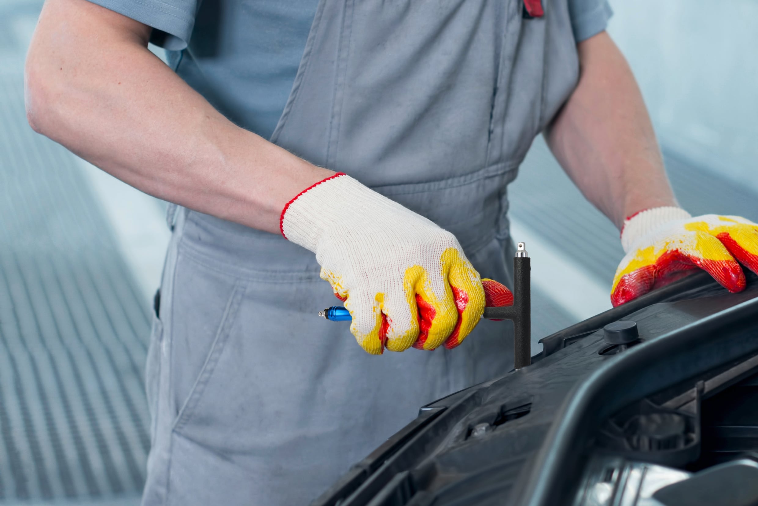 Een persoon repareert een auto-onderdeel, houdt een schroevendraaier vast en draagt handschoenen.