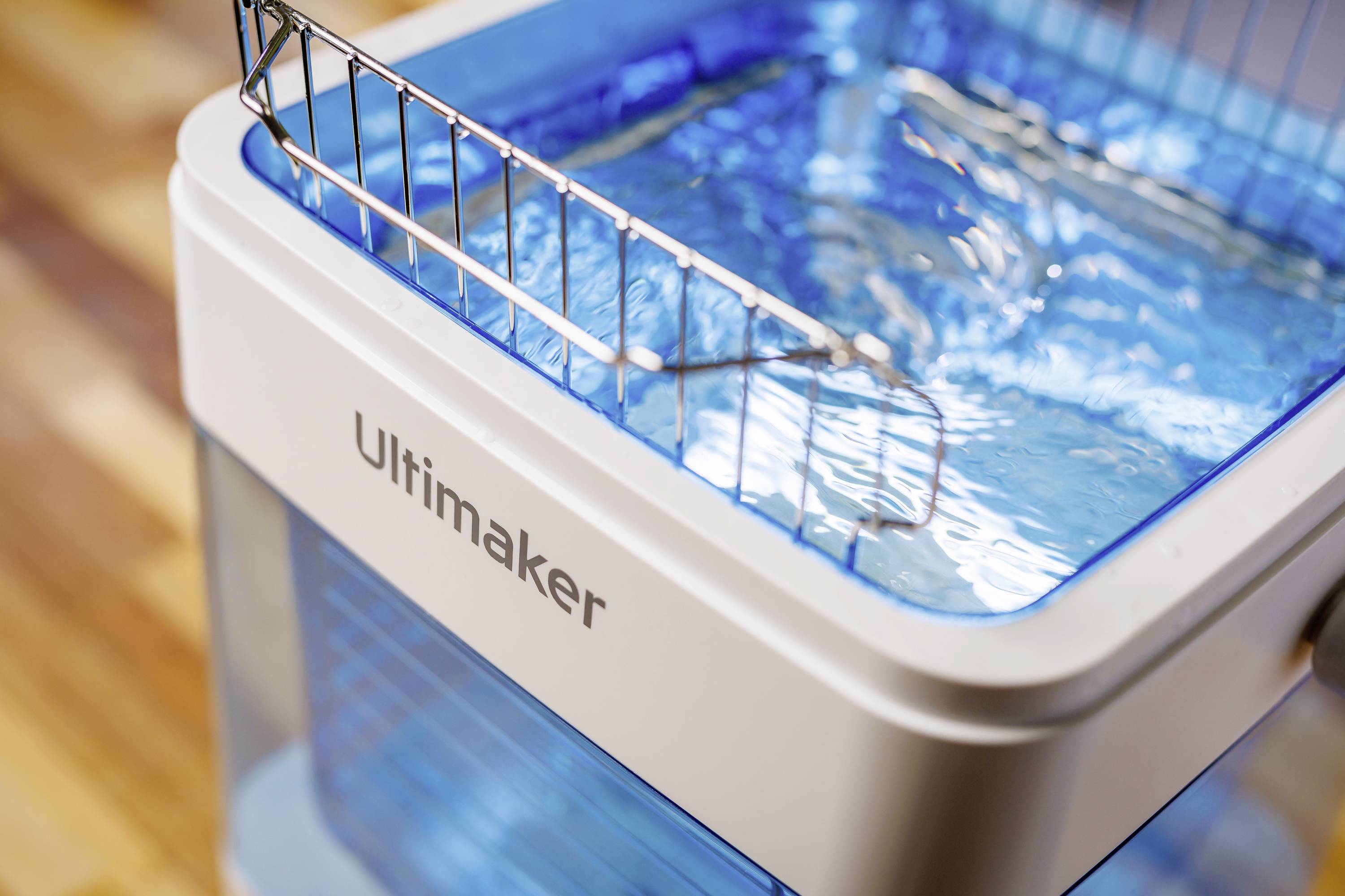 Een 3D-printer met de naam 'Ultimaker', gevuld met blauw water, staand op een houten vloer.