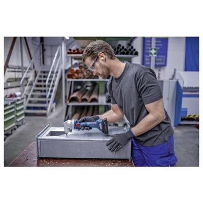 Werknemer die een draadloos elektrisch gereedschap gebruikt om de rand van een metalen plaat in een industriële werkplaats te snijden of af te smoothen.
