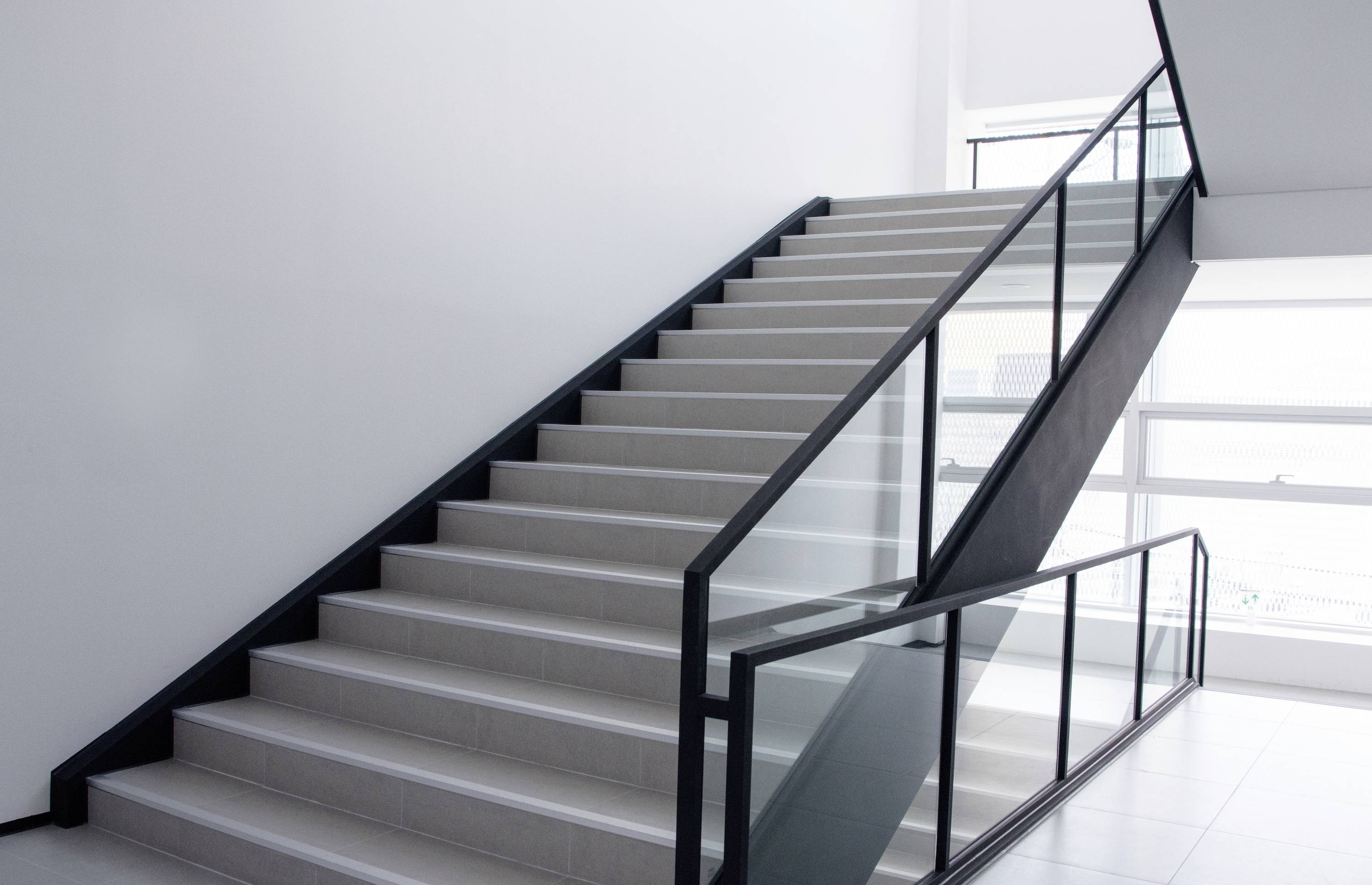 Een moderne trap met zwarte leuning en glazen balustrade in een lichte, minimalistische ruimte. Daglicht stroomt binnen door grote ramen.