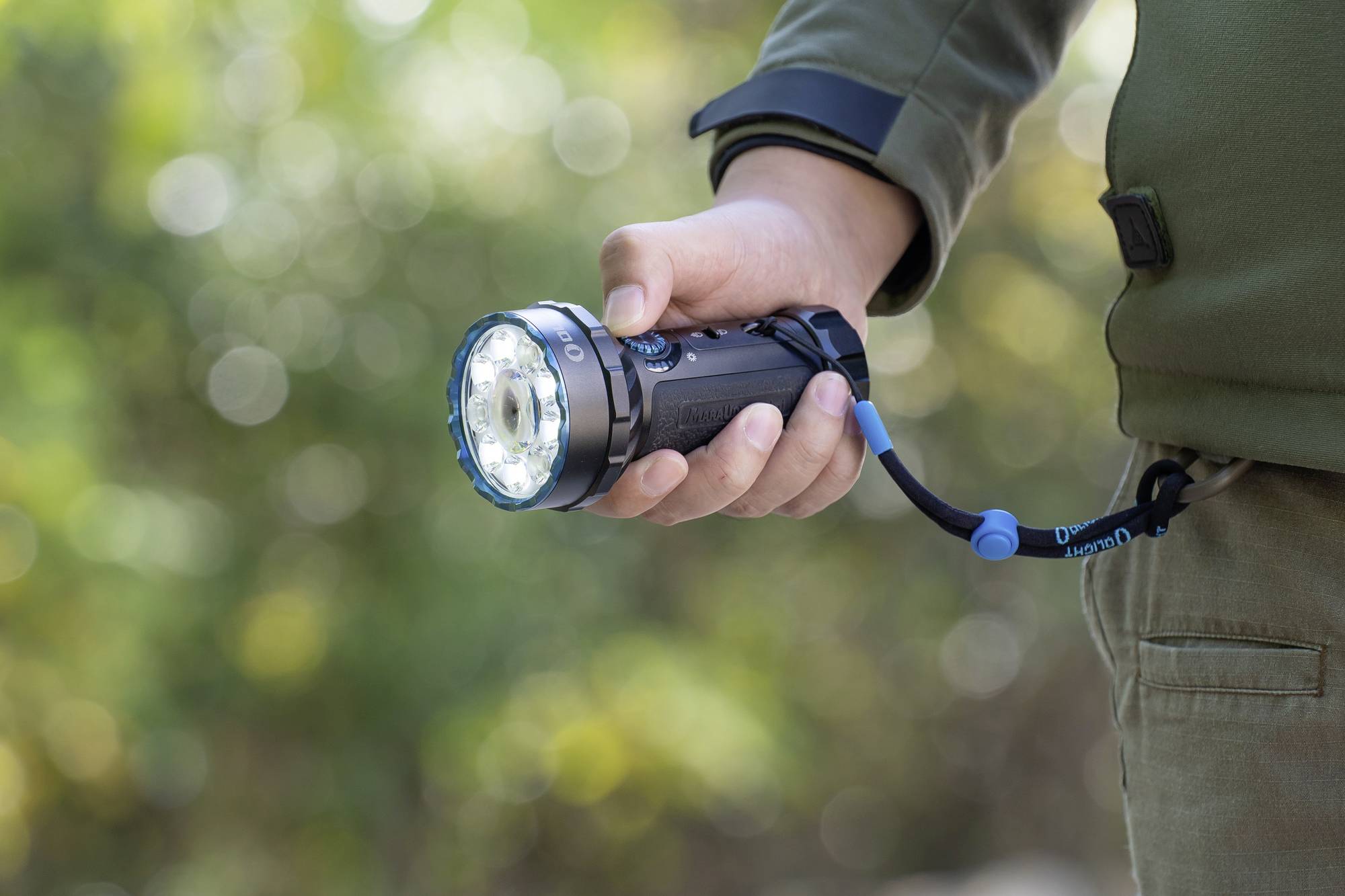 Een persoon houdt een zaklamp in de hand. De zaklamp schijnt helder en heeft een blauw lint. De achtergrond is onscherp.