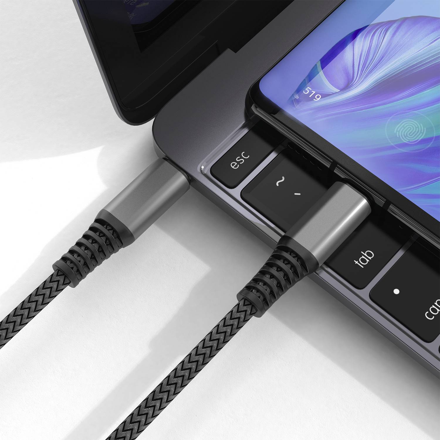 Een smartphone ligt schuin over het toetsenbord van een laptop, beide verbonden met gevlochten oplaadkabels.