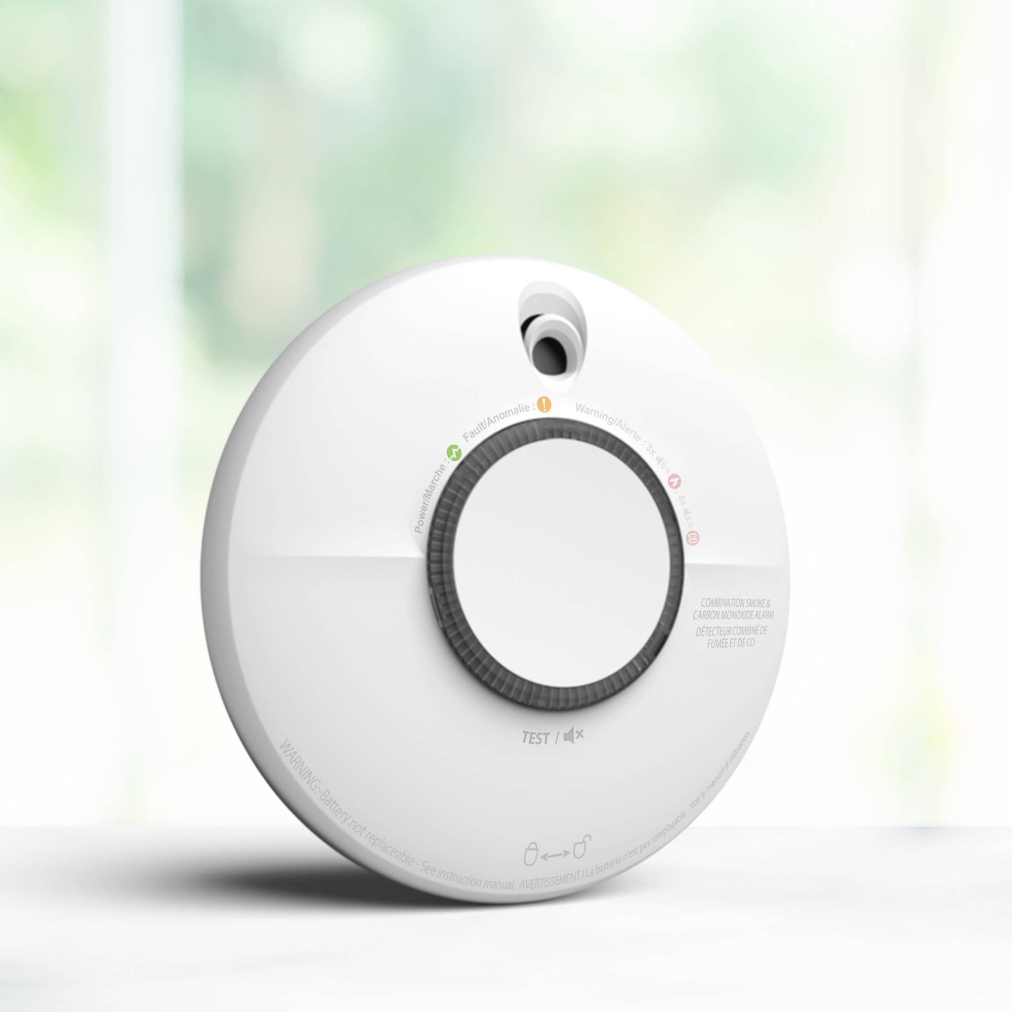 Een rookmelder in close-up met een grote centrale knop en led-indicatoren voor status. Achtergrond is onscherp.