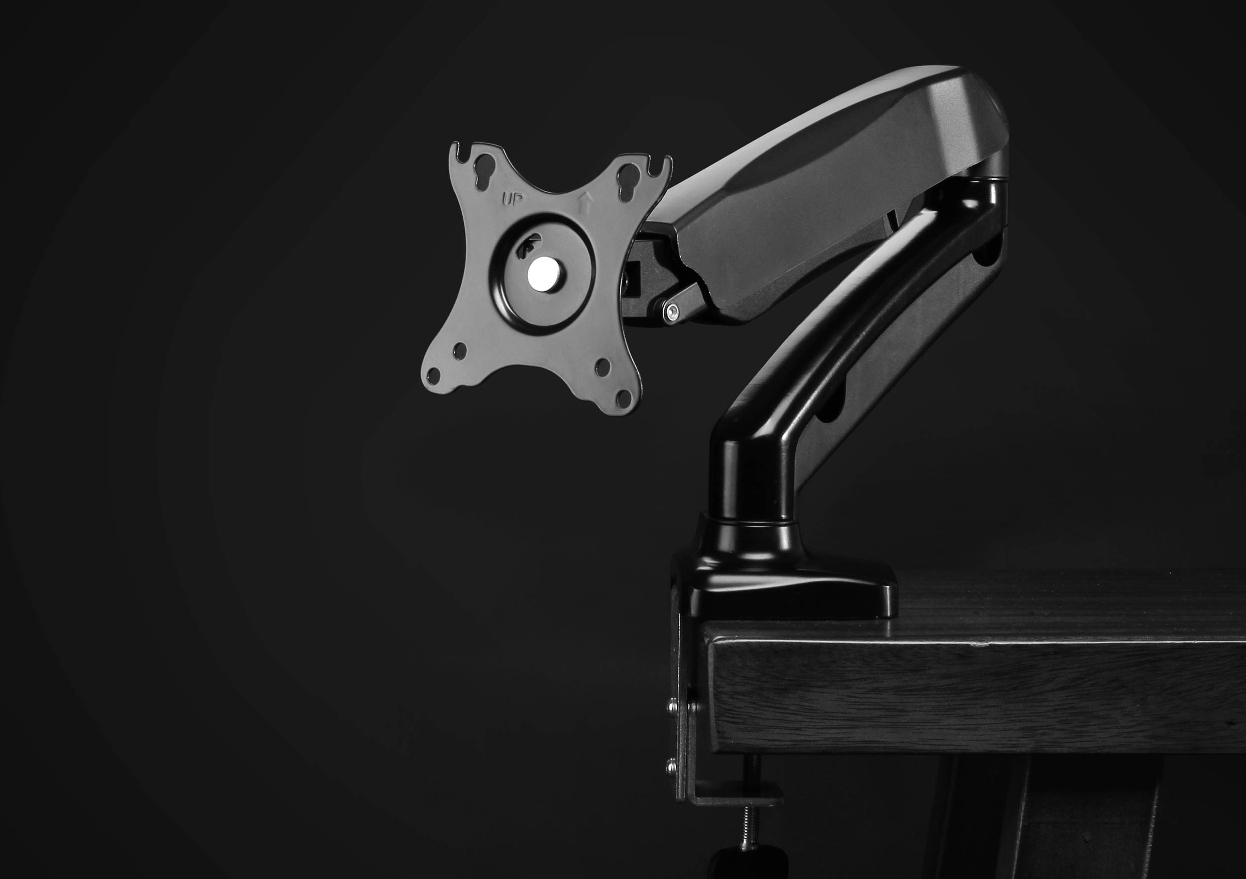 Een zwarte monitorarm zonder beeldscherm is aan een bureau gemonteerd. De arm is flexibel en verstelbaar.