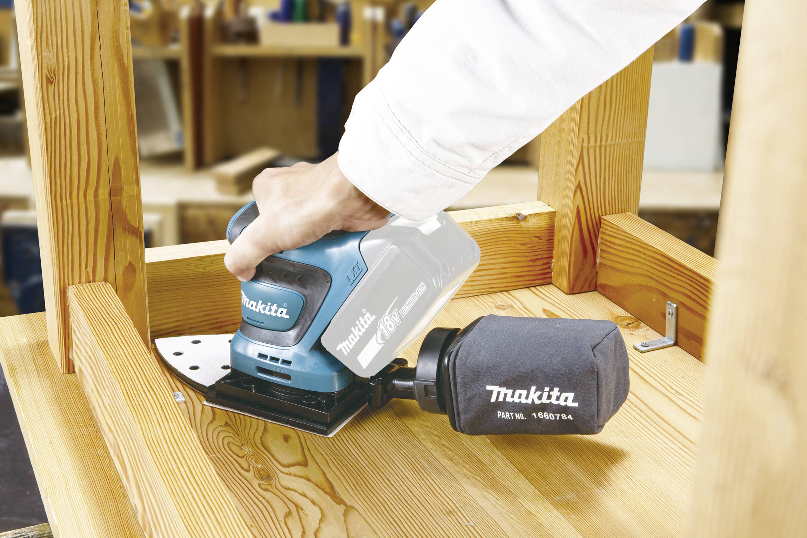 Een persoon schuurt een houten oppervlak met een Makita-schuurapparaat om het oppervlak glad en bewerkt te maken.