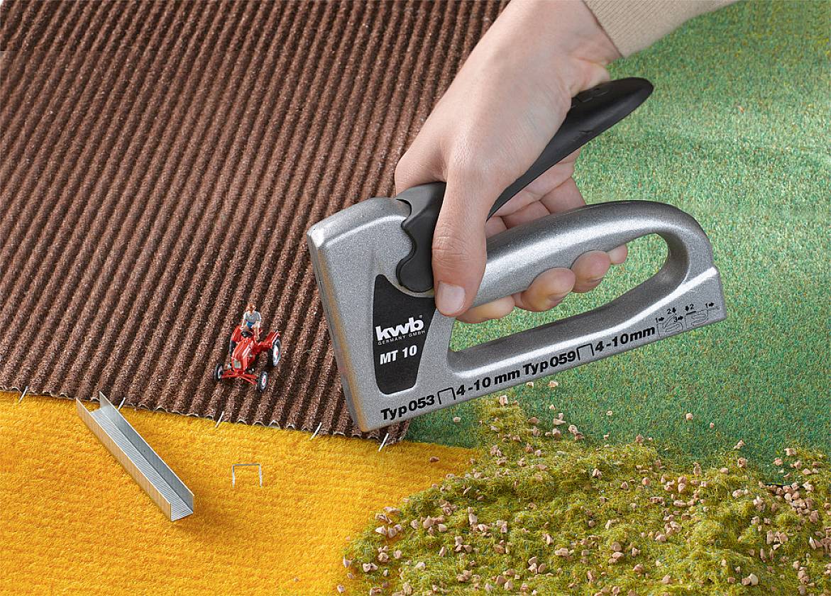 Een hand gebruikt een nietmachine om verschillende tapijtstalen met elkaar te verbinden. Verschillende texturen zijn zichtbaar.