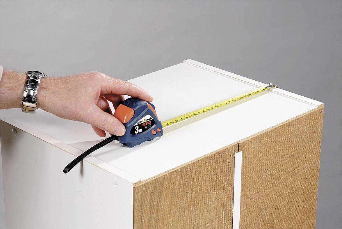 Een hand meet de breedte van een kast met een meetlint dat 30 centimeter aangeeft.