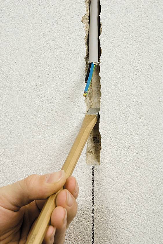 Een persoon trekt een elektrische kabel uit een gleuf in de muur met behulp van een houten steel.