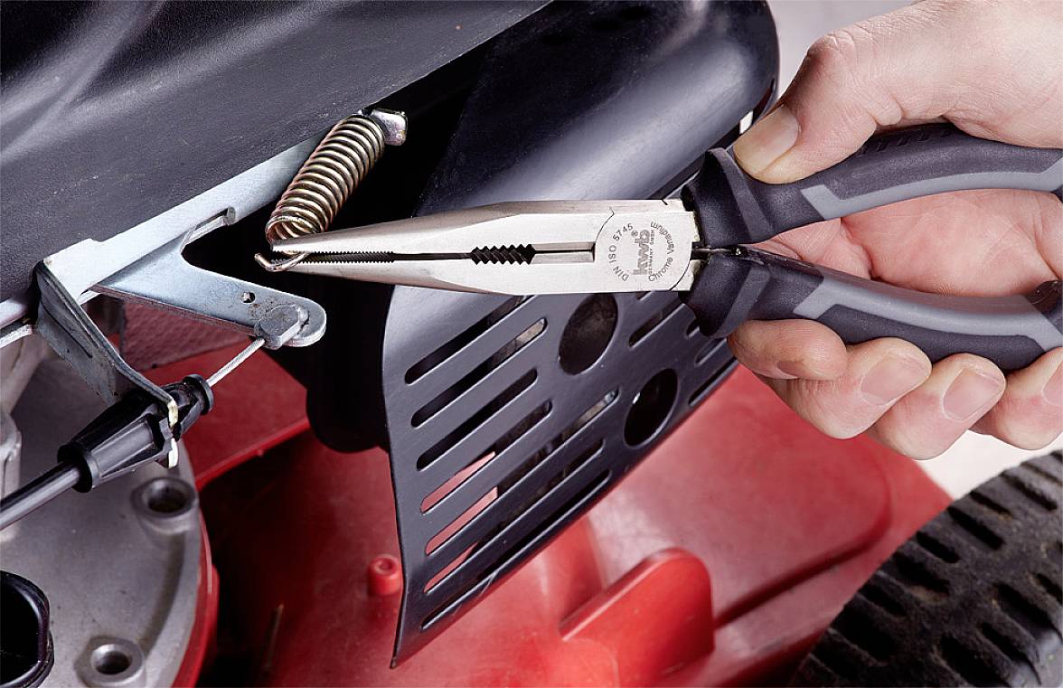 Een hand houdt een tang vast en werkt aan een veer in een apparaat, waarschijnlijk voor onderhoud of reparatie.