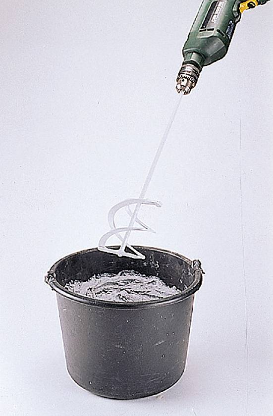 Een boormachine met roervoorziening mengt een stroperige grijze massa in een zwarte emmer.