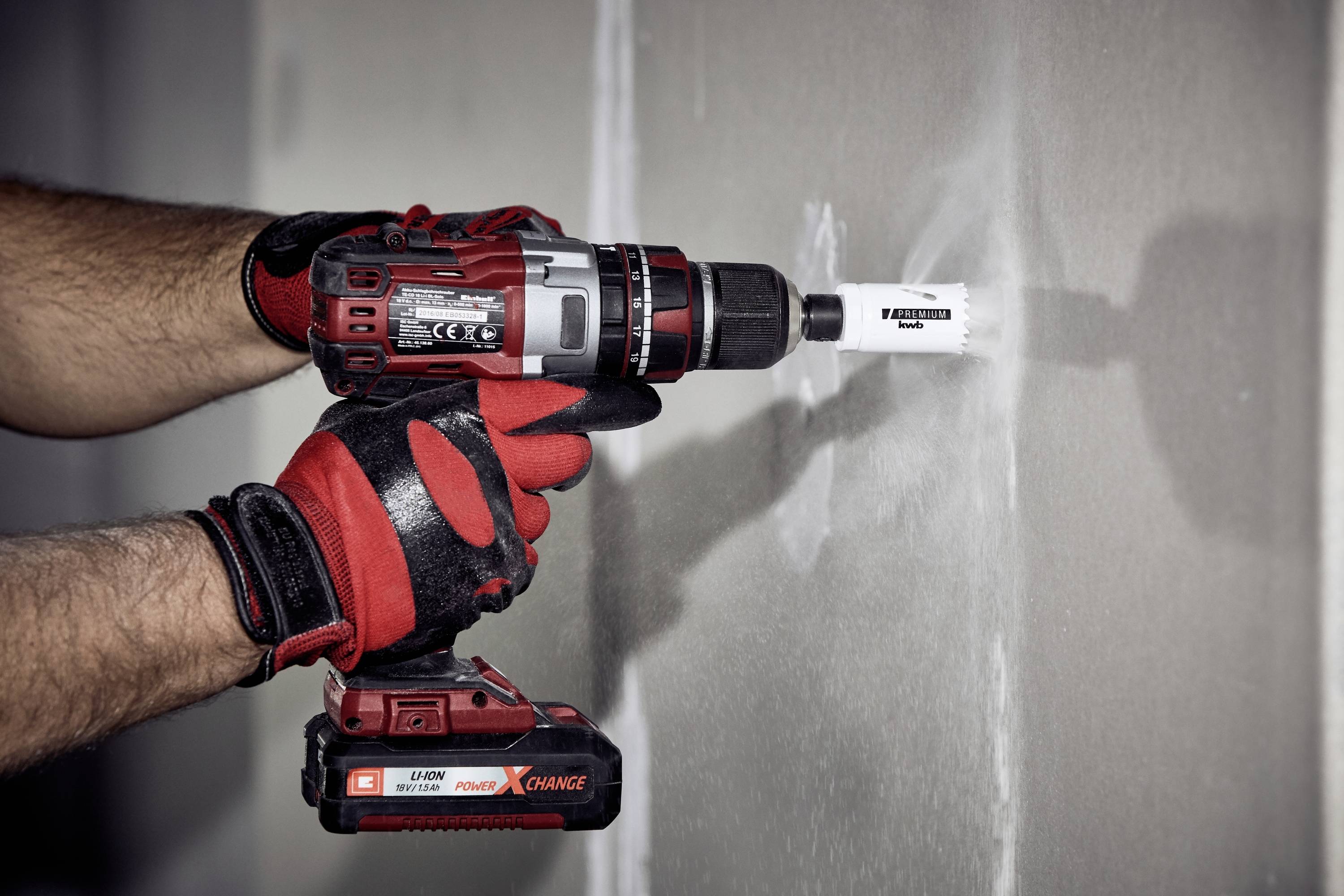 'Een persoon gebruikt een rode boormachine om een gat te boren in een witte muur. Beschermende handschoenen worden gedragen.'