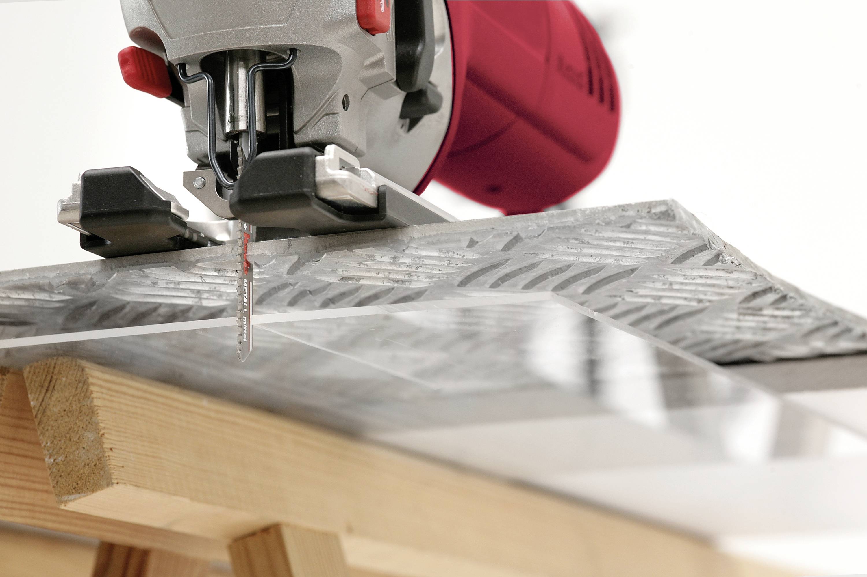Elektrische decoupeerzaag snijdt een dun metalen plaatje op een houten tafel; gedetailleerde close-up van het zaagblad en het metaal.