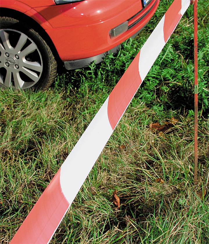 Rode auto geparkeerd naast een rood-witte afzetting op een grasveld.