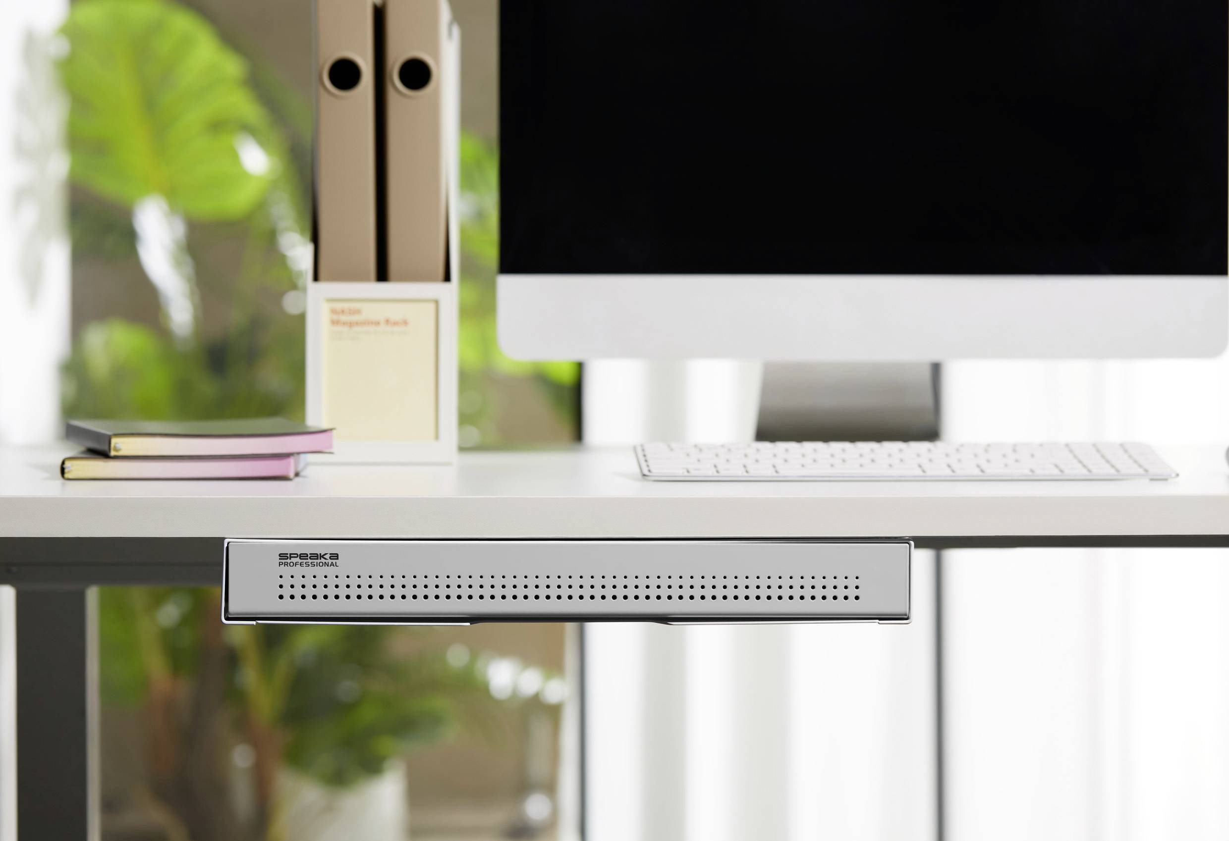 Een moderne bureau met een computerscherm, toetsenbord, ordners en planten op de achtergrond.