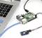 Een Raspberry Pi, via een netwerkkabel verbonden met een laptop, naast een kleine sensor met kleurrijke kabels op een witte achtergrond.