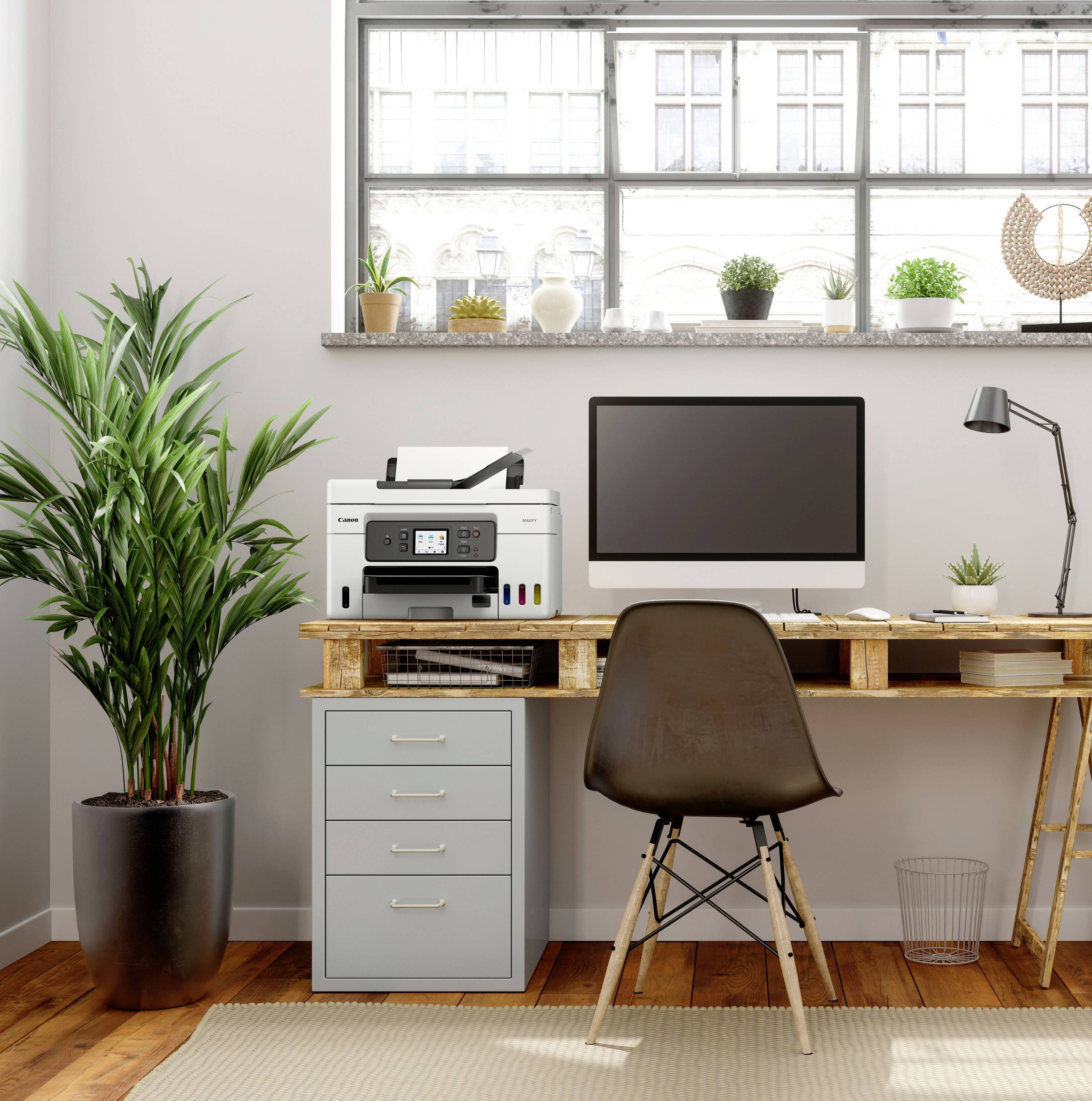 Een bureau met computer, printer en lamp voor een groot raam. Naast het bureau staat een plant, met daaronder een grijze archiefkast.