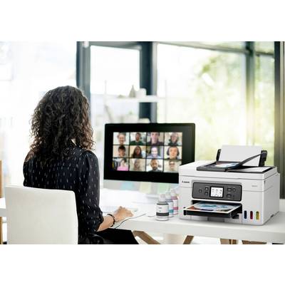 Een persoon zit aan een bureau en gebruikt een computer voor een videoconferentie. Naast haar staat een printer met gedrukte foto's.
