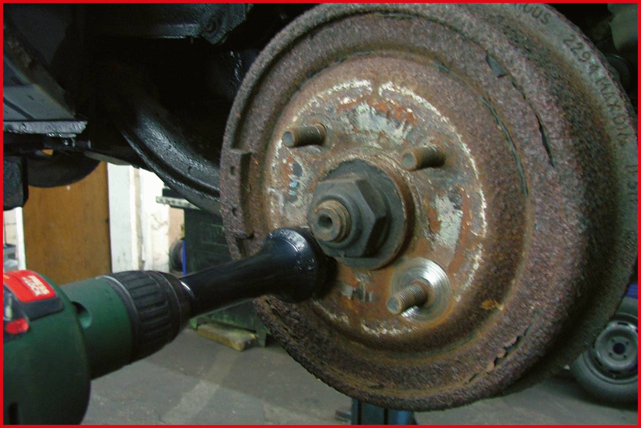 Een verroest autoremwiel wordt bewerkt met een elektrisch gereedschap. De afbeelding toont een werkplaatscontext.