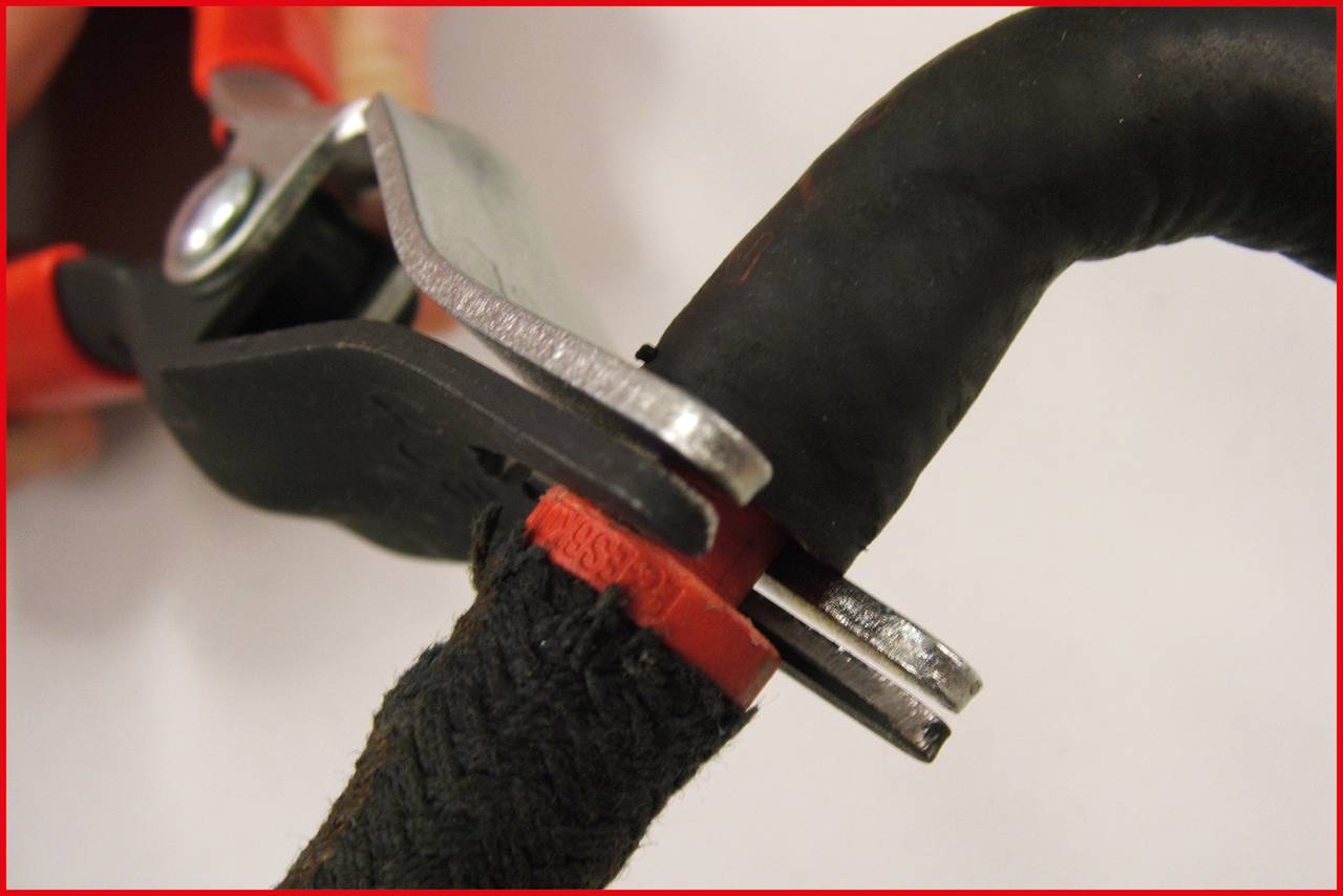 Een rode tang knipt een dik, zwart kabel met een rode beschermmantel.