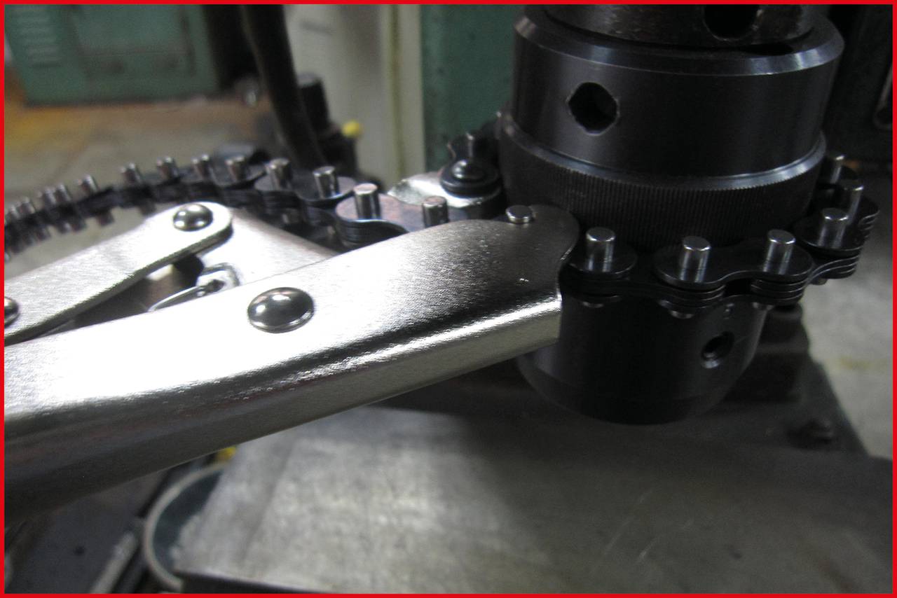 Een close-up van een mechanisch apparaat met ketting en tandwiel. De metalen onderdelen ogen stevig en industrieel.